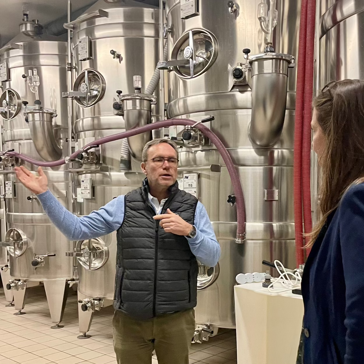 Olivier Belin i sit tank rum, hvor champagnen produceres, fortæller Louise Søborg, med ryggen til, om sine champagne. 3 vin ståltanke i baggrunden.