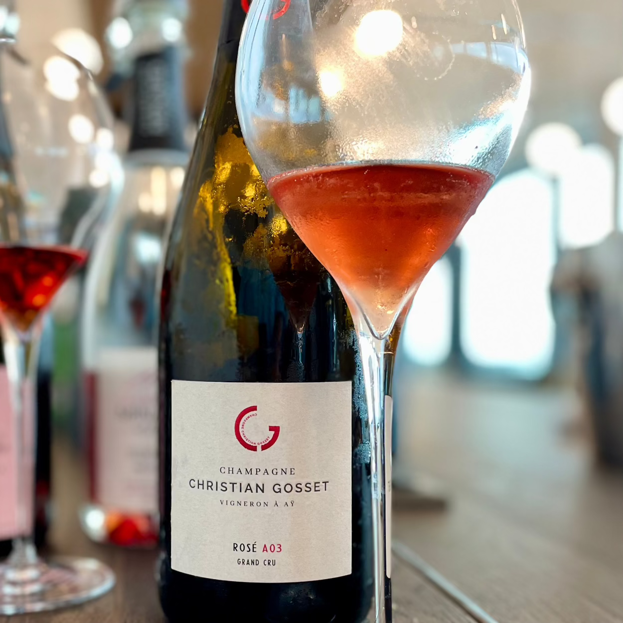 Champagneflaske på bord med champagneglas foran fyldt med rosé champagne, Champagne Christian Gosset, Rosé A03, Grand Cru