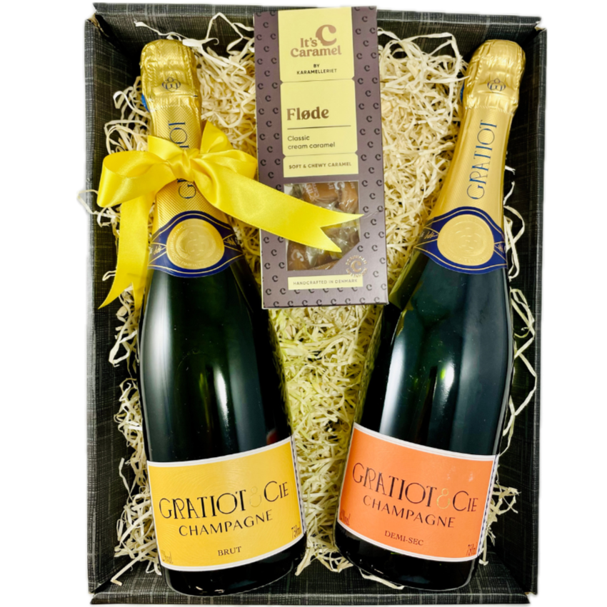 2 flasker champagne og 1 pakke flødekarameller i gavekasse med træ-fnuller. Champagne Gratiot & Cie, Almanach no. 1, Demi-sec og Brut, sidstnævnte med en gul sløjfe om halsen