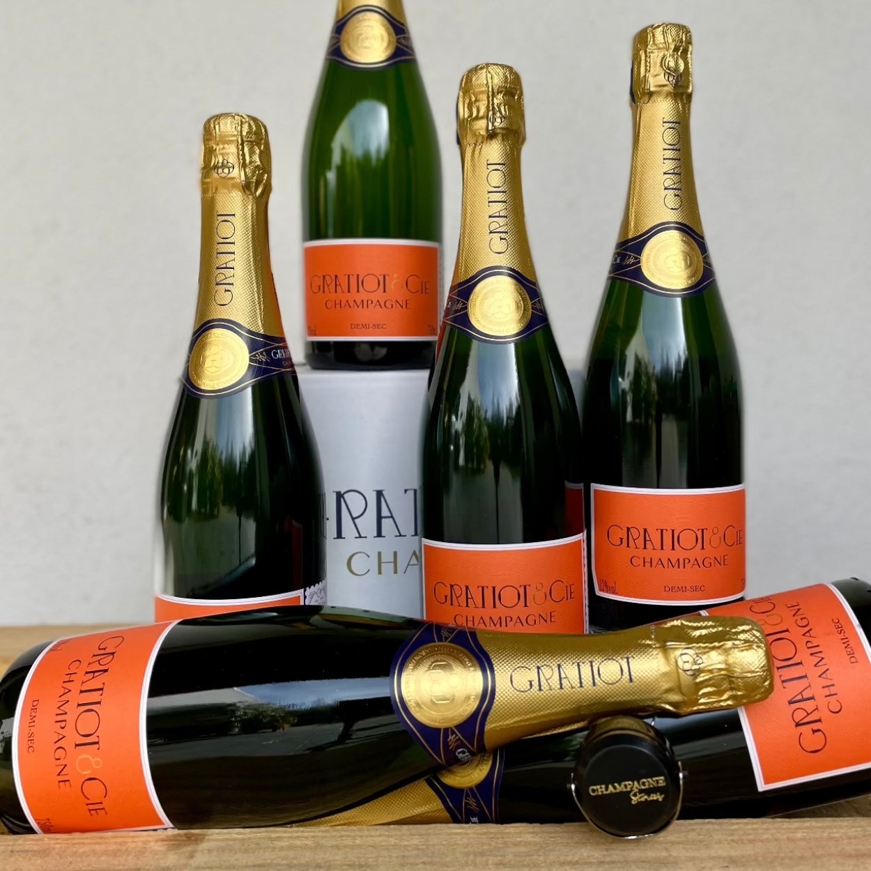 2 liggende og 4 stående flasker champagne på hvid baggrund fra Champagne Gratiot & Cie, Demi-Sec, orange etikette, champagnestopper med logo "Champagne Stories"