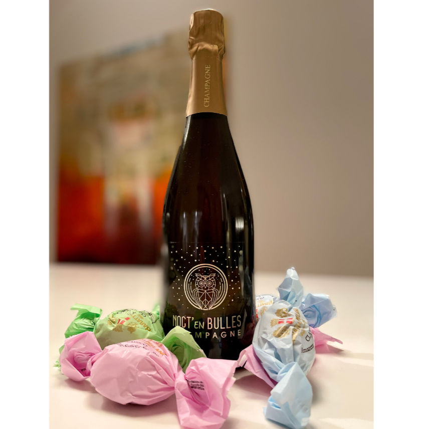 Champagne flaske på bord med små indpakket kager i lyserødt, grønt og blåt papir, Champagne Piot-Sévillano, Noct'en Bulles, Demi-Sec