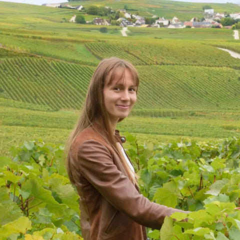 Portræt af Virginie Bergeronneau ståenden ved vinranker fra Champpagne Virginie Bergeronneau med vinmarker i baggrund