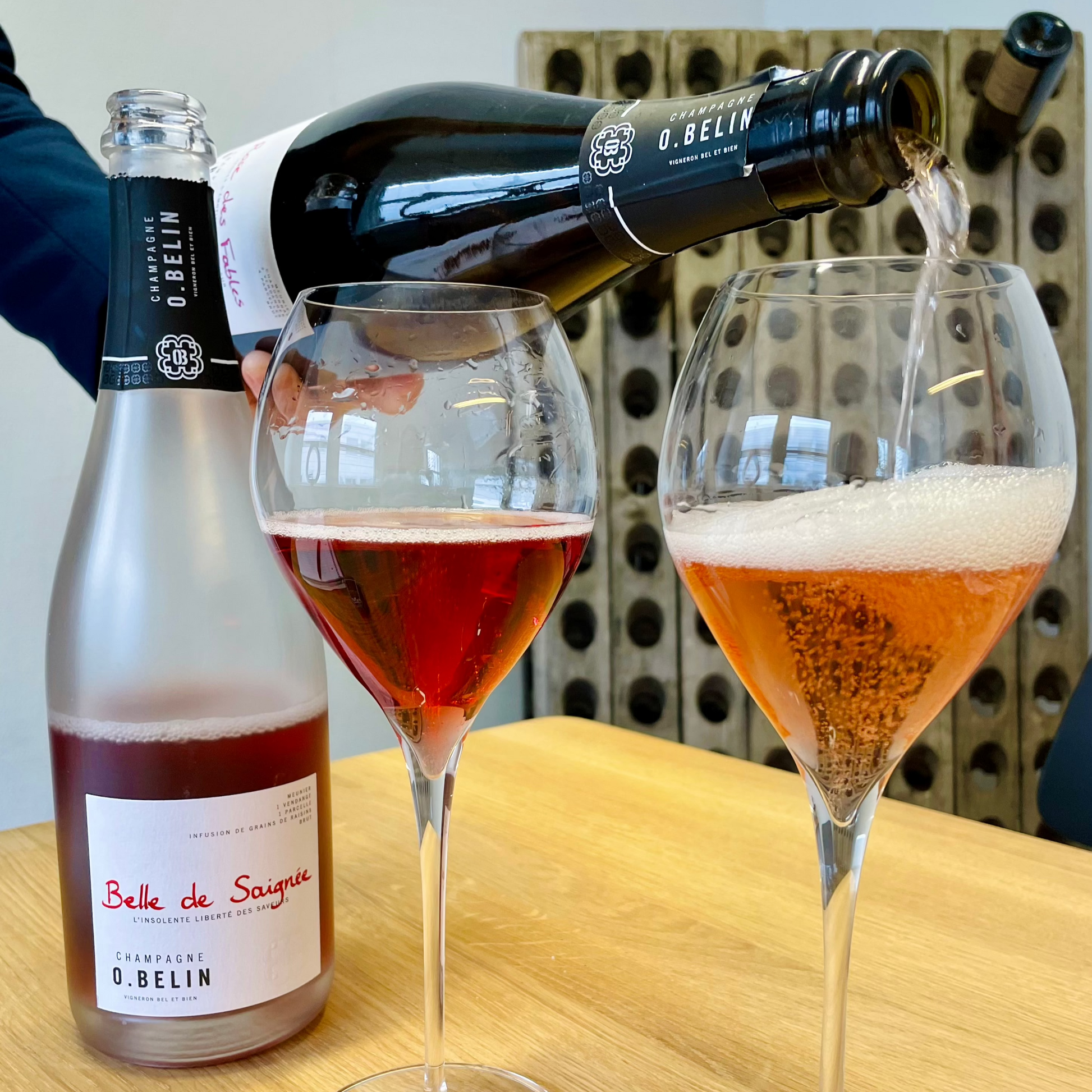 2 flasker roséchampagne hvor af der skænkes fra den ene flaske og 2 champagneglas med roséchampagne. Champagne O. Belin, Belle de Saignée og Rose des Fables. Pupitre i baggrunden