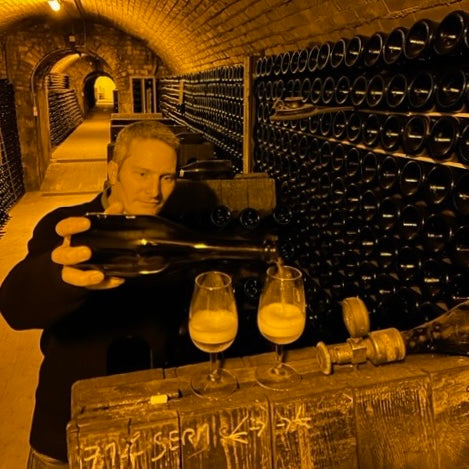 Billed fra kælderen hos Champagne Francois Secondé. Ejer Jérôme Groslambert servere 2 glas champagne, mange flasker ligger på hylder i baggrunden