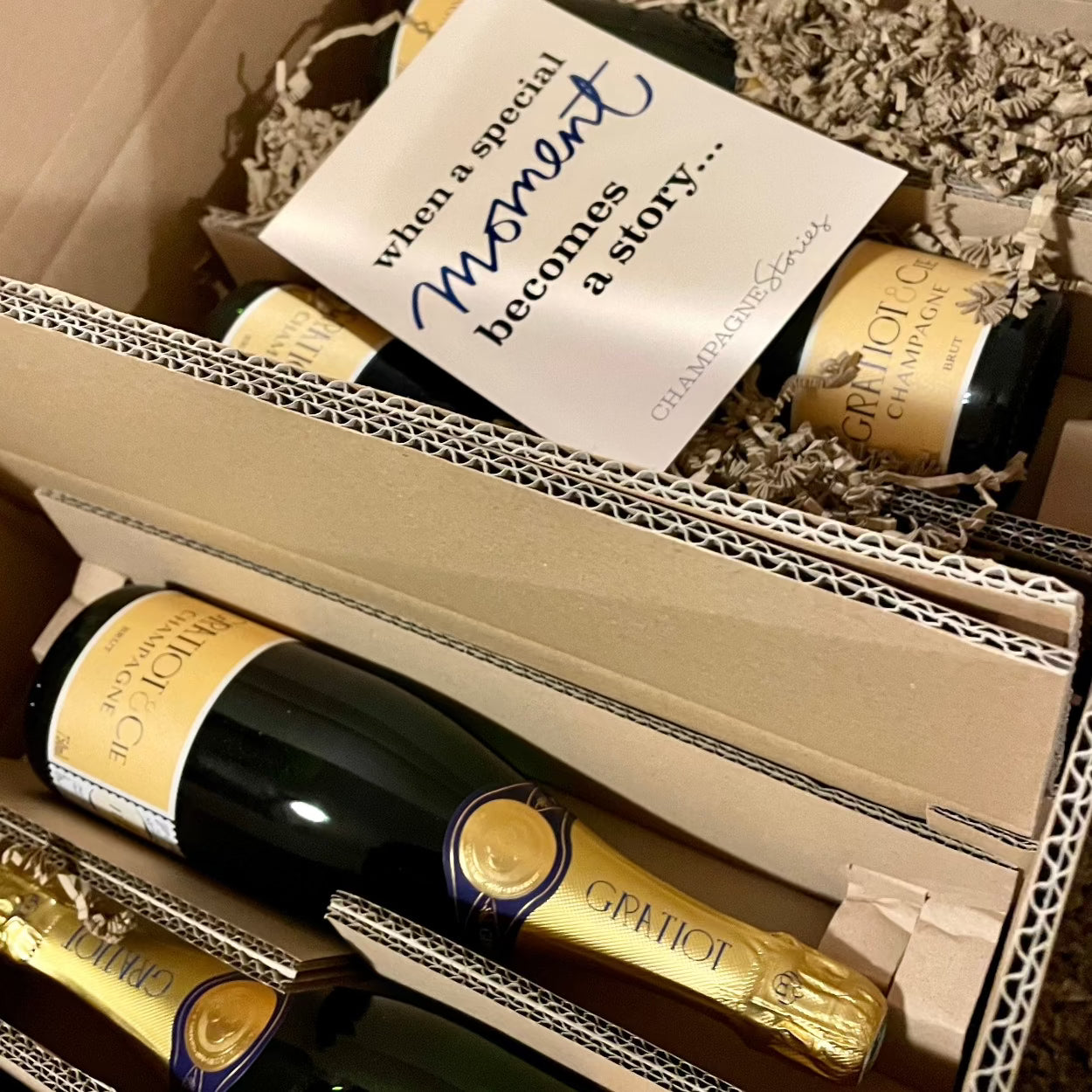 flere flasker champagne fra Champagne Gratiot & Cie, Brut, gul etikette, ligger i forsendelses kasser, et postkort med teksten "when a speciel moment becomes a story..." ligger henover nogle af flaskerne