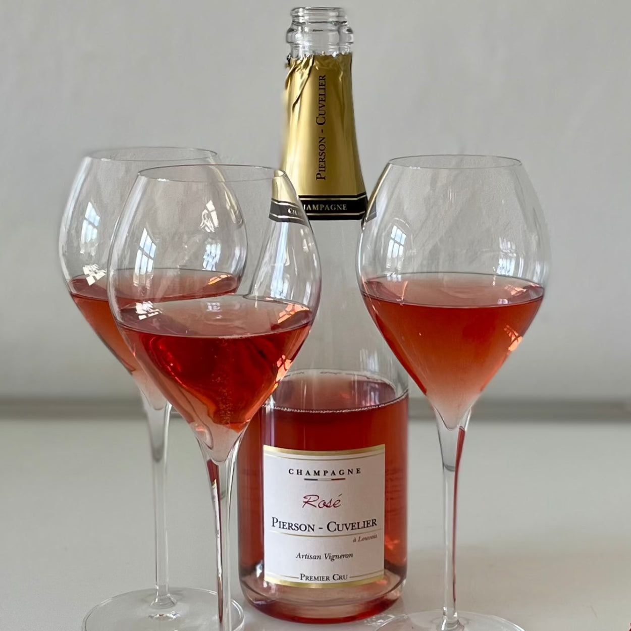 1 flaske rosé champagne fra Champagne Pierson-Cuvelier, Rosé, Premier Cru, omgivet af 3 Lehmann Grand Jamesse champagneglas med rosé champagne, hvid baggrund