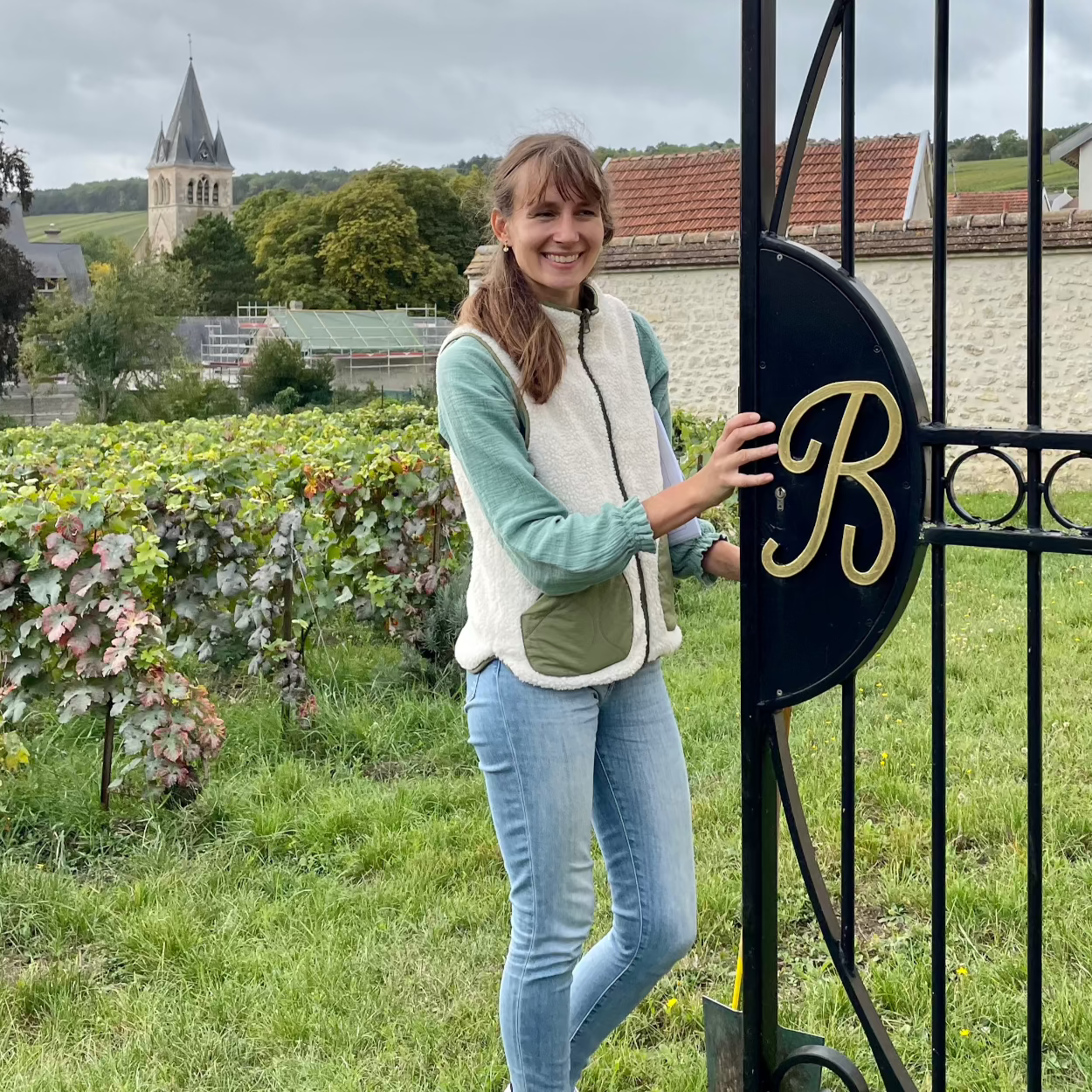 Virginie Bergeronneau ved lågen til familiens Clos - vin mark og kirke i baggrund