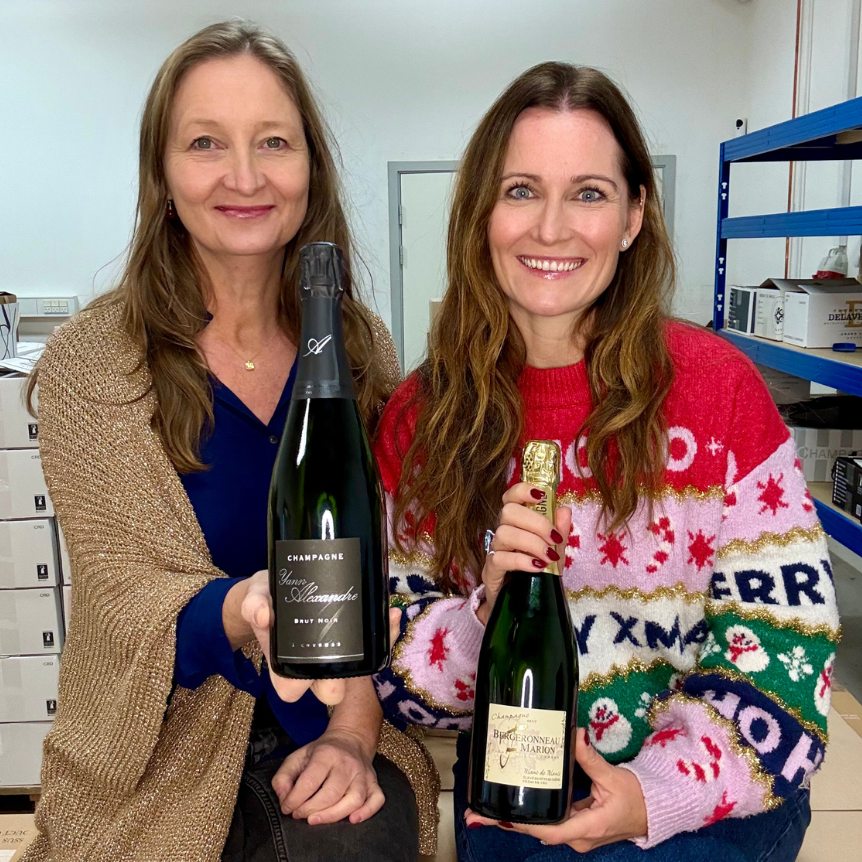 Louise Søborg og Louise Herping i julesweater med hver deres flaske champagne. Champagne Yann Alexandre, Brut Noir og Champagne F. Bergeronneau-Marion, Blance de Blancs