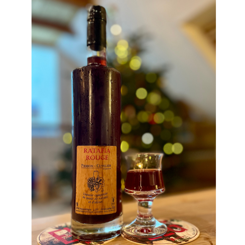 1 flaske Ratafia Rouge, likør fra Champagne Pierson-Cuvelier, ved siden et lille glas med Ratafia Rouge, uskarp baggrung af juletræ